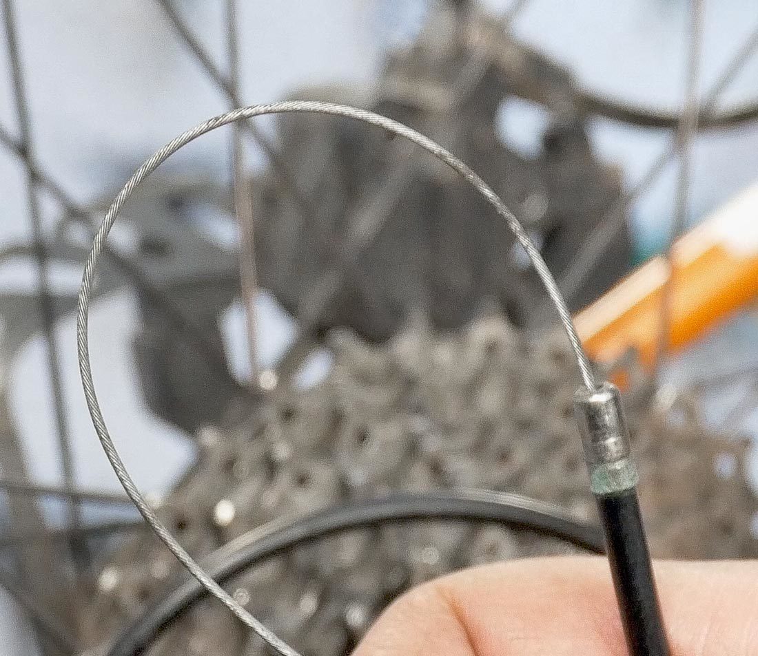 Ręce odkręcające śrubę mocującą starą linkę w przerzutce tylnej roweru